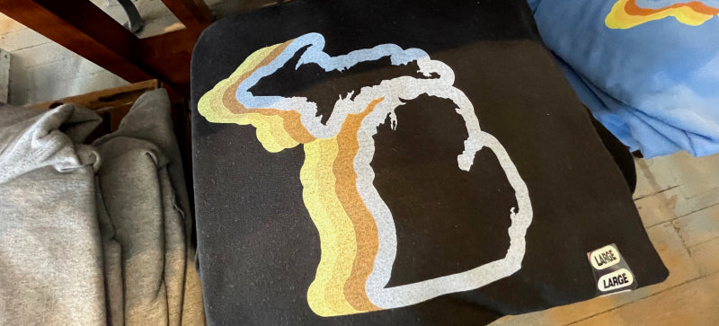 Michigan 70's sweatshirt by Enjoy Michigan - Black sweatshirt with a yellow orange color wave outline of the state of Michigan